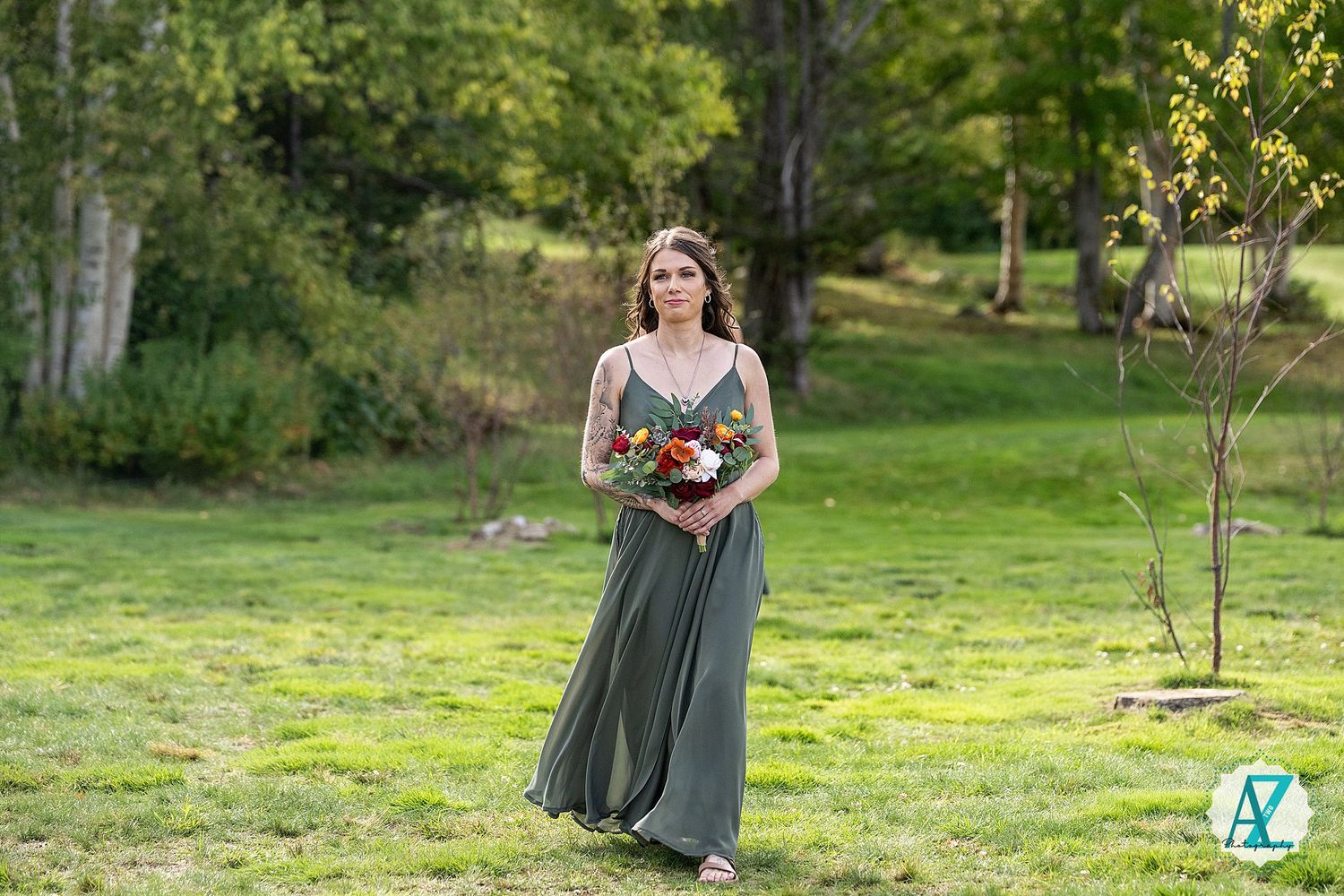 Someone wearing a sage green dress walks in a sunny garden with flowers and trees in the background.