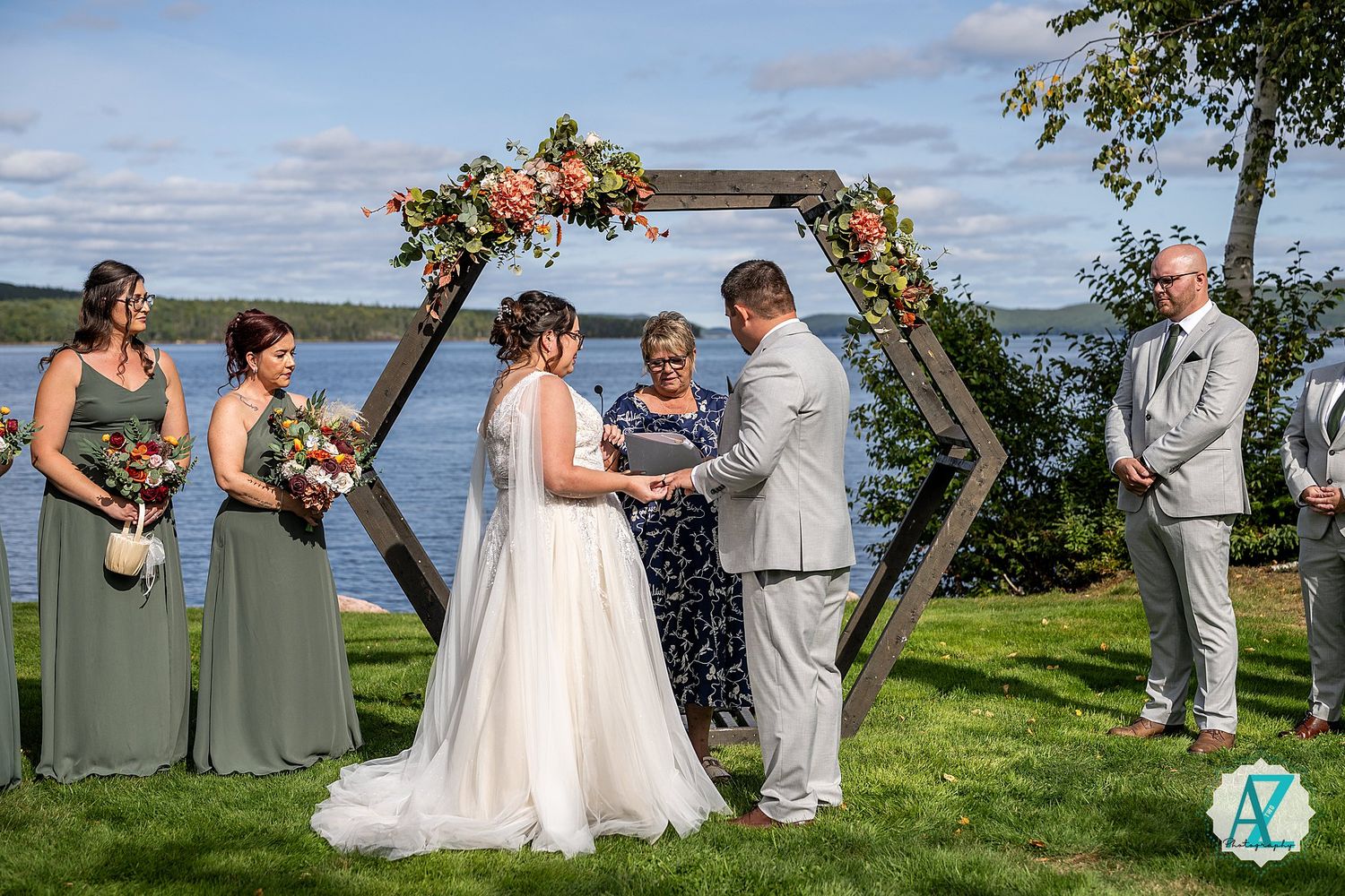 Outdoor waterfront wedding ceremony with guests seated on chairs under cloudy skies by the bay.