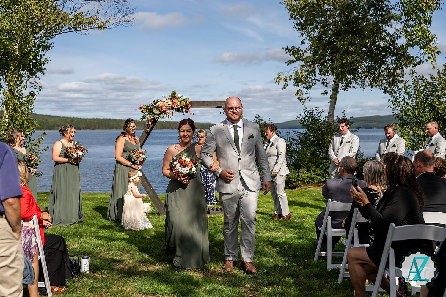 Wedding ceremony set up on grassy lawn overlooking lake with white chairs and natural scenery.
