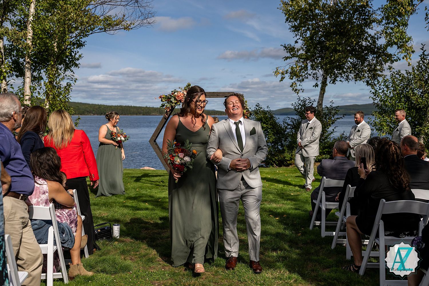 Wedding guests mingle during an outdoor reception with lake and trees in the background.