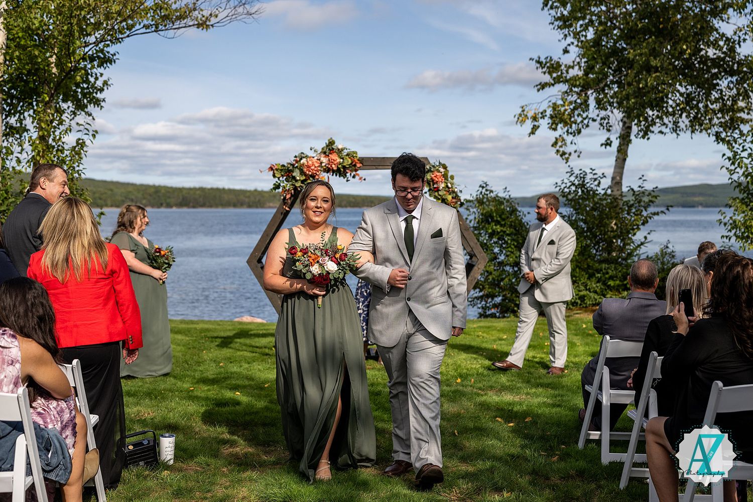 Scenic lakeside wedding celebration with guests gathered on lawn under blue skies.