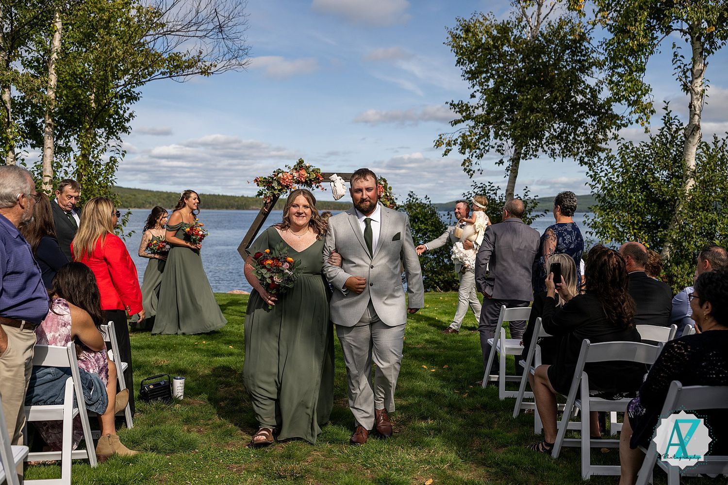Small wedding ceremony on a sunny day with seats arranged outdoors while attendees gather at a hilltop location.