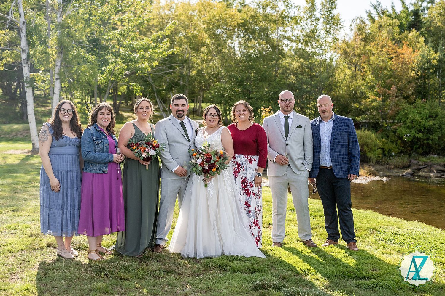Wedding party poses together for formal group photos outdoors in golden afternoon sunlight on a grassy lawn.