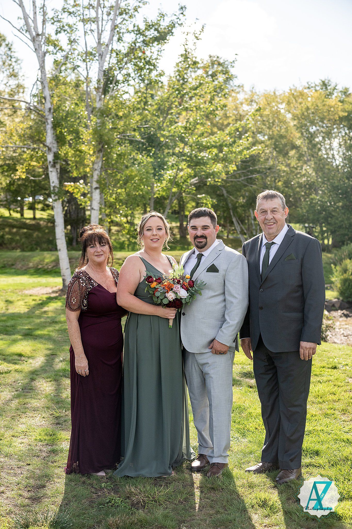 Wedding party members pose together on a sunny day in a grassy outdoor setting.