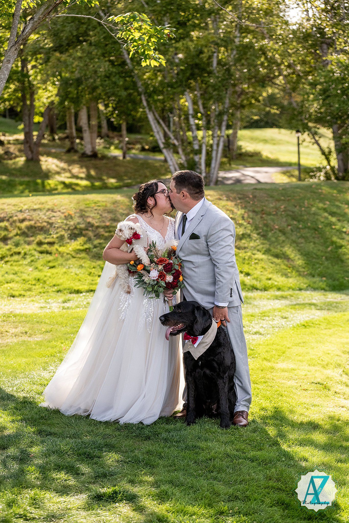 A couple shares a romantic moment on their wedding day with their black dog in a sunlit park setting.