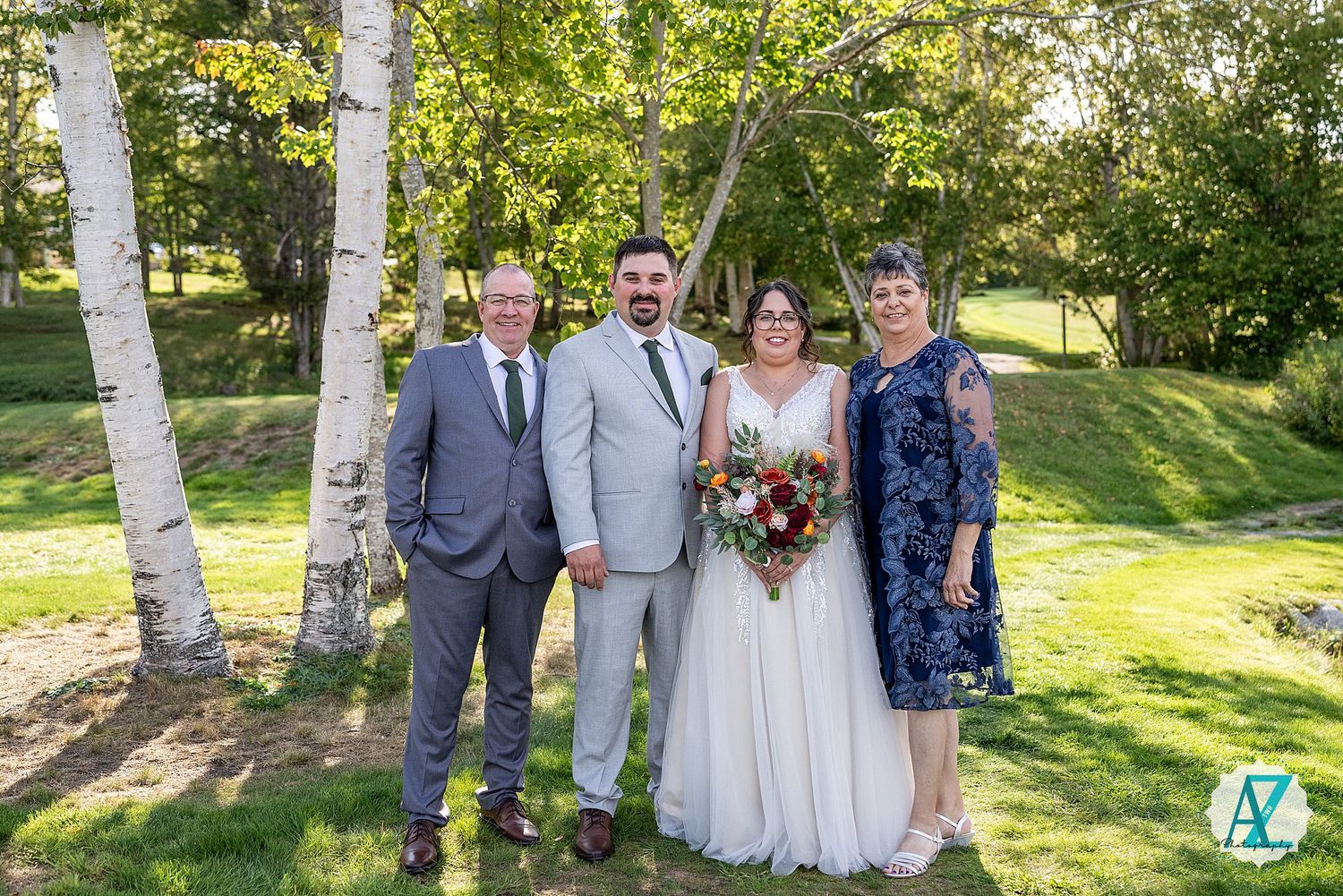Wedding party poses together on grassy lawn with birch trees in the background during golden hour.