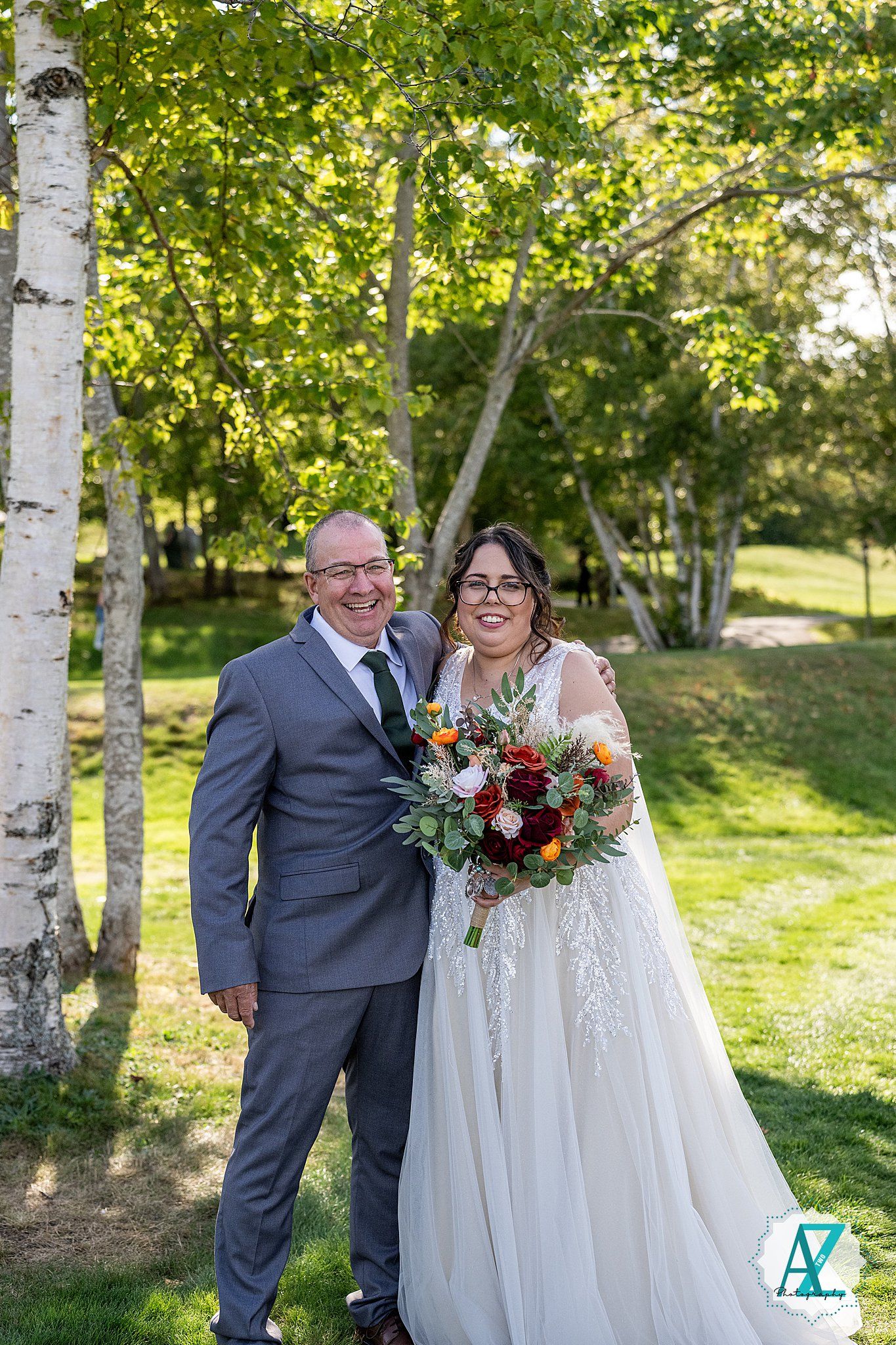 A romantic wedding photo features a couple embracing among birch trees in a sunlit garden setting.