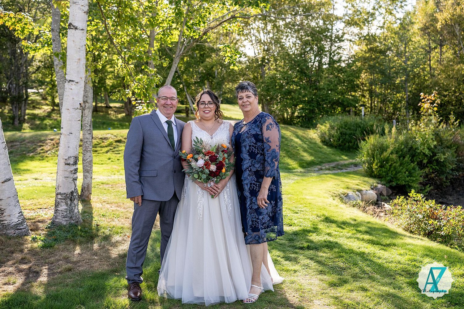 Wedding party poses outdoors in natural setting surrounded by birch trees and green foliage.