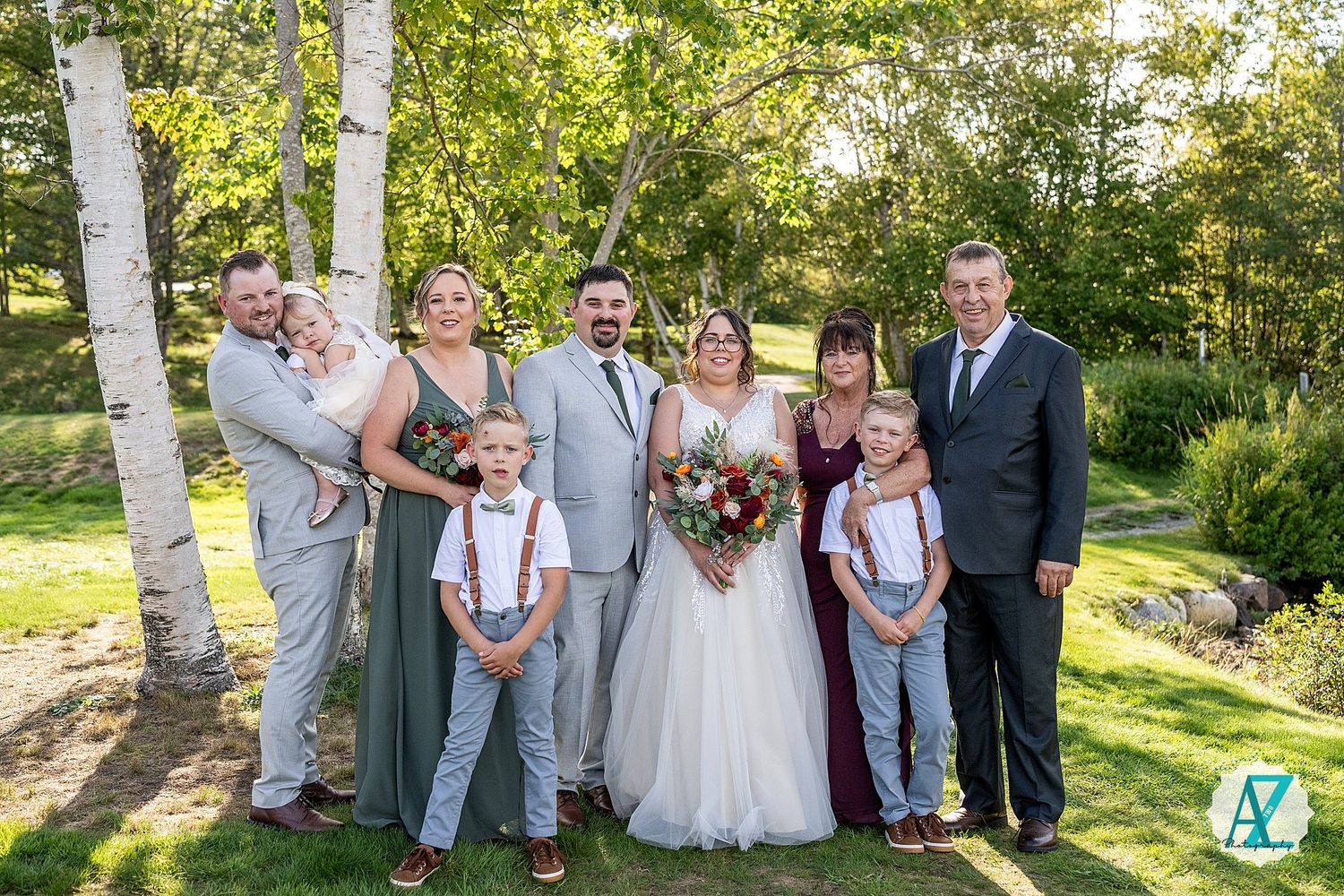 Wedding party poses for portraits between birch trees on a sunny afternoon in a garden setting.