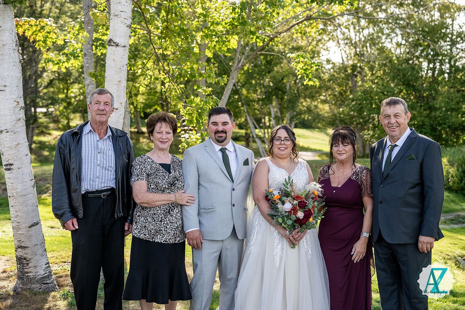 Wedding party poses outdoors under birch trees in a garden setting on a sunny day.