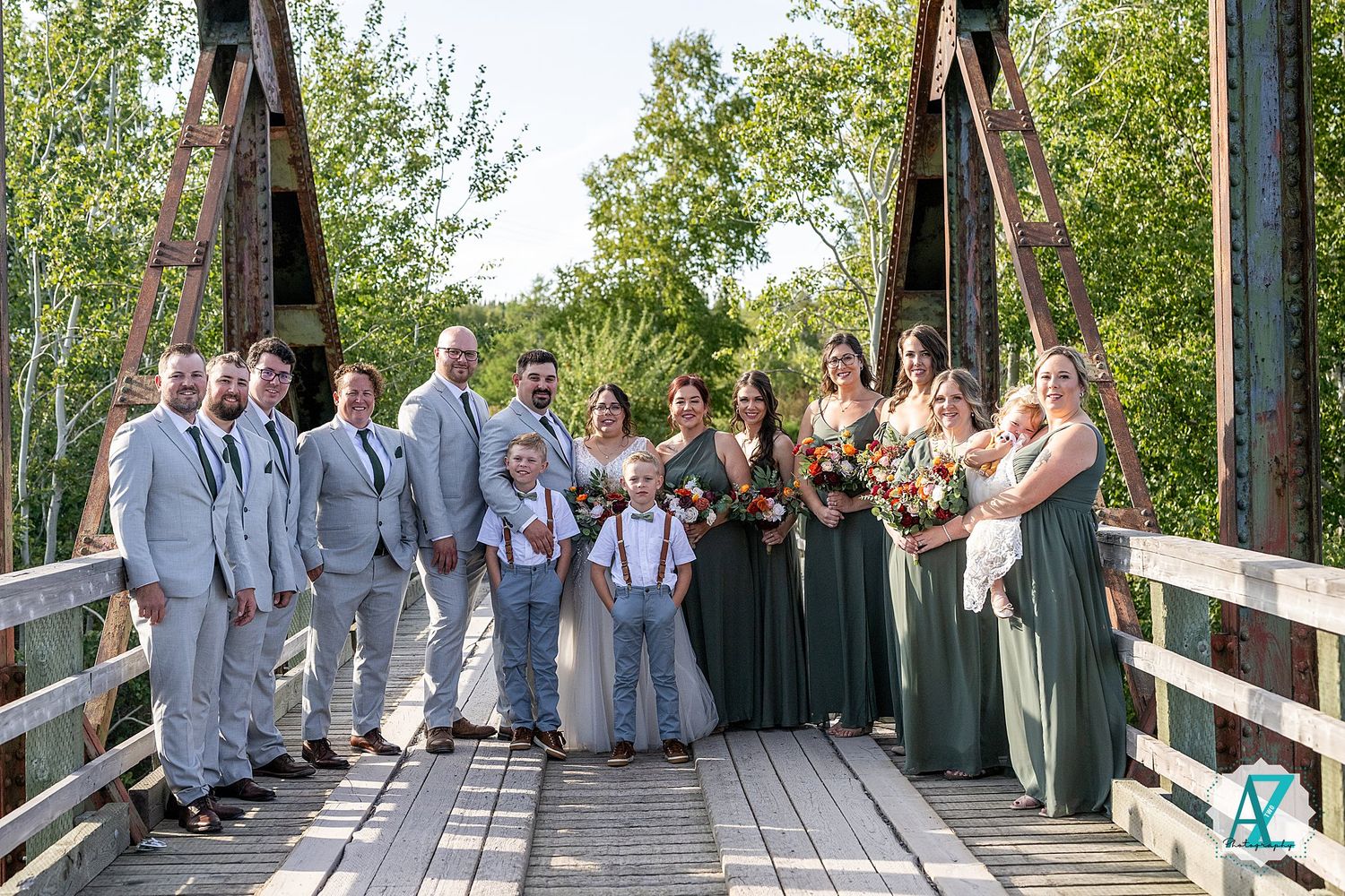 Long wooden bridge in a park setting with wedding attendees lined up in formal attire for photos.