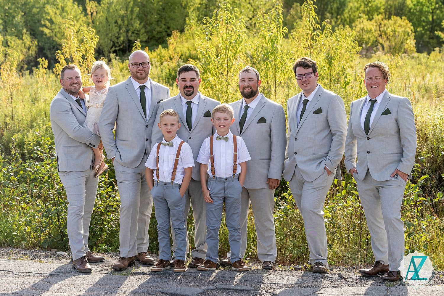 Wedding party in gray suits and suspenders poses together against yellow wildflower backdrop in outdoor setting.