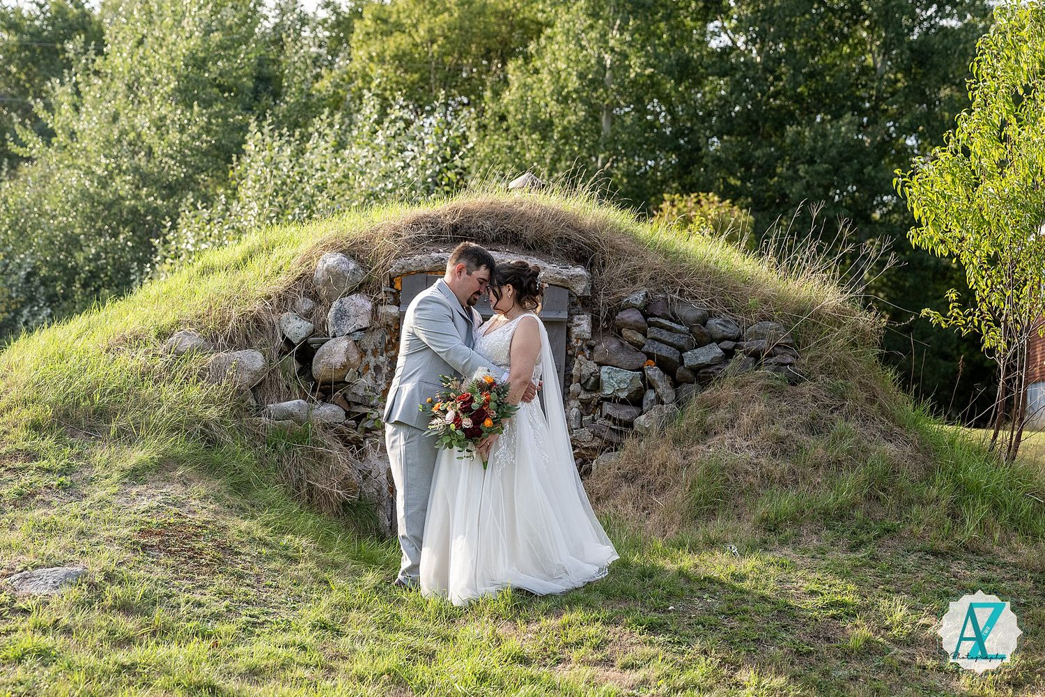 Couple in wedding attire poses together on grassy hillside path during outdoor photo session.
