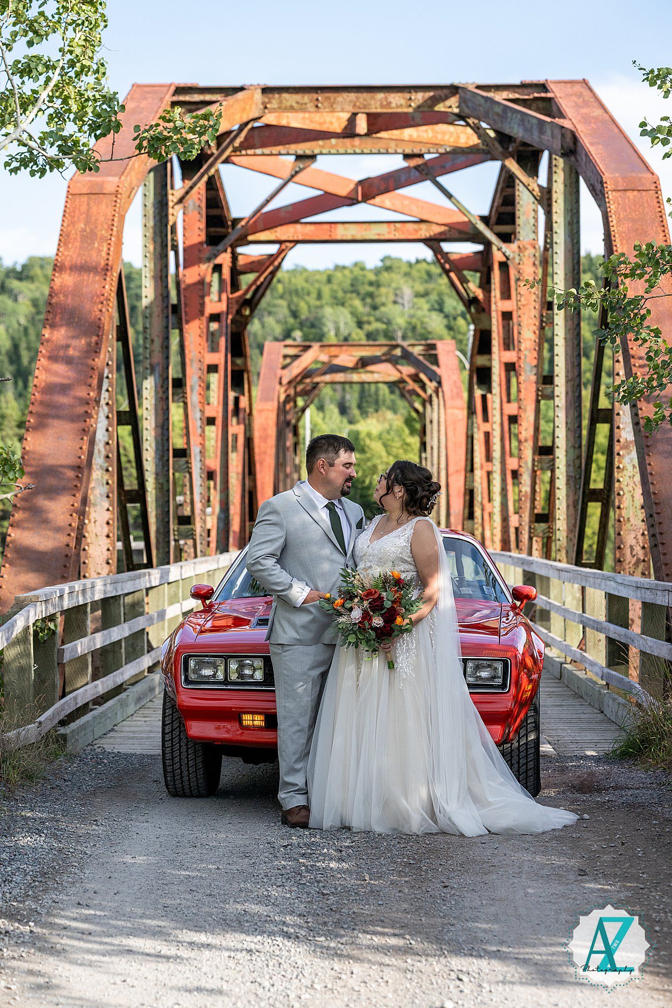 Newlyweds share intimate moments on a rustic wooden bridge with a vintage red truck in the background during sunset.