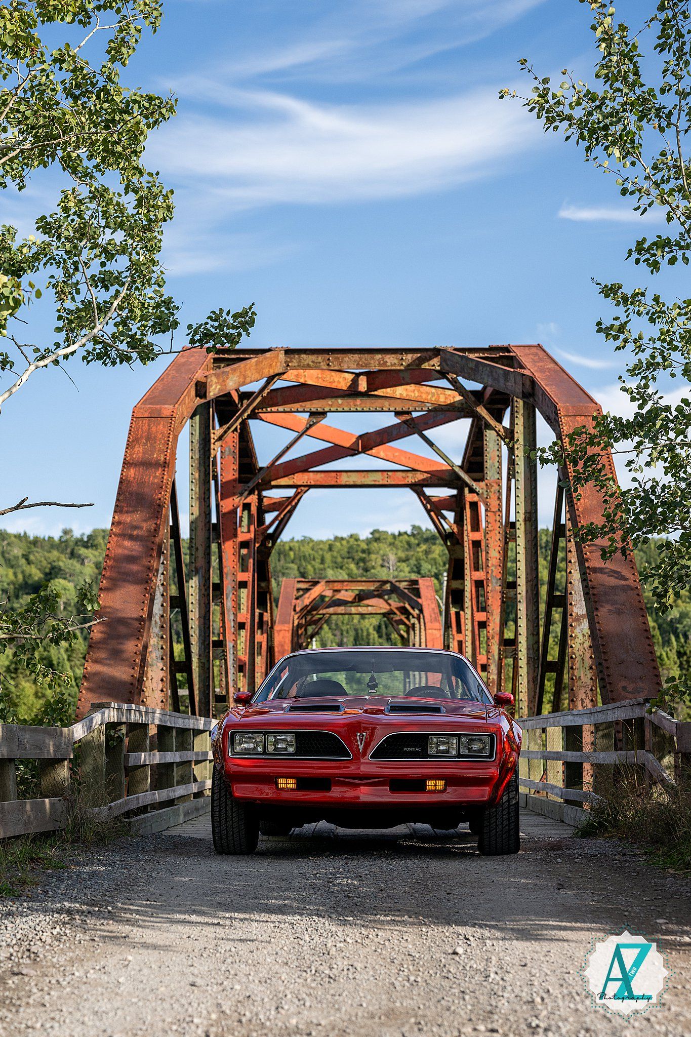 Classic red Pontiac Trans Am photographed from different angles on a rustic metal bridge surrounded by green trees.