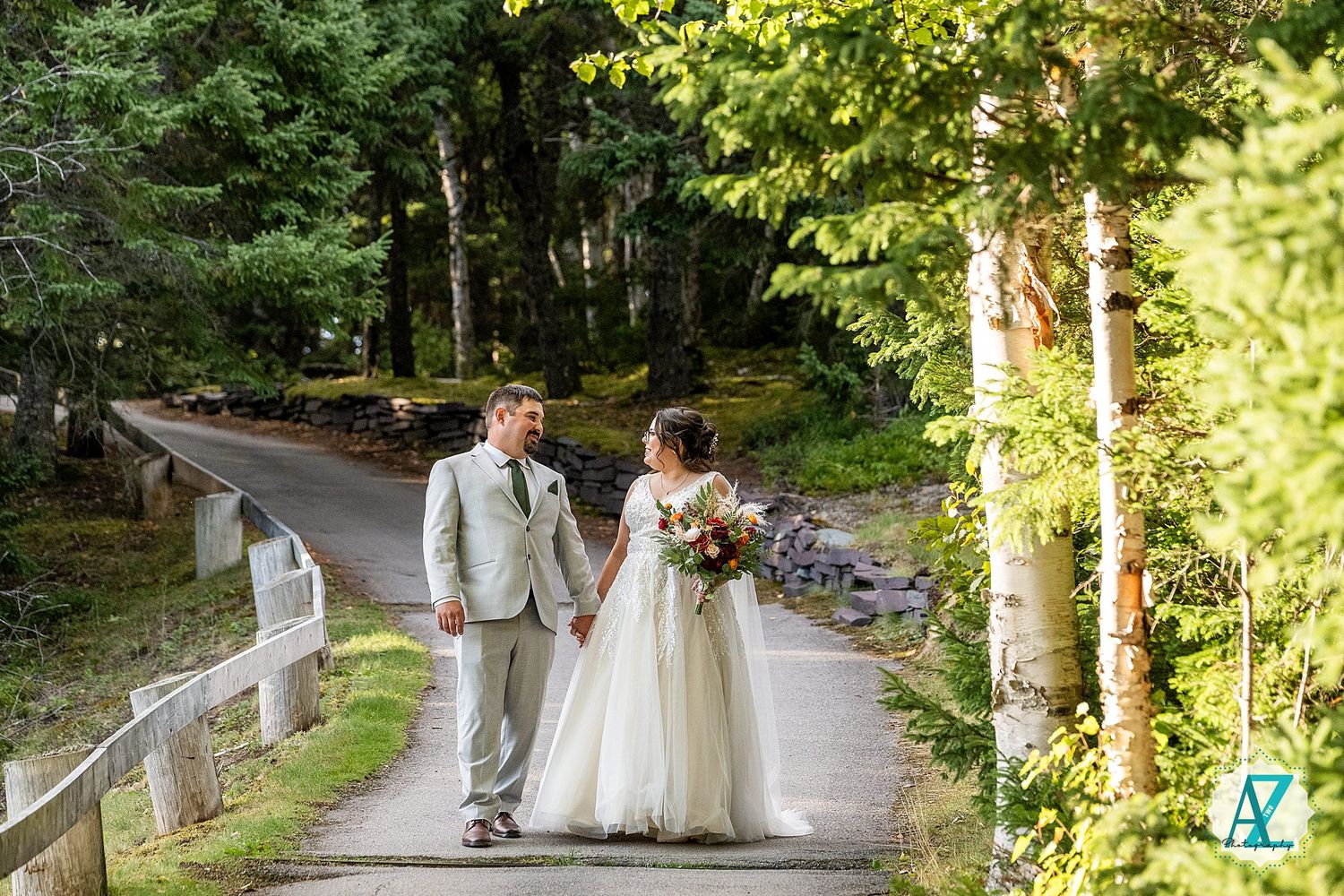 Wedding couple walks along a scenic forest path surrounded by lush greenery and sunlit trees.