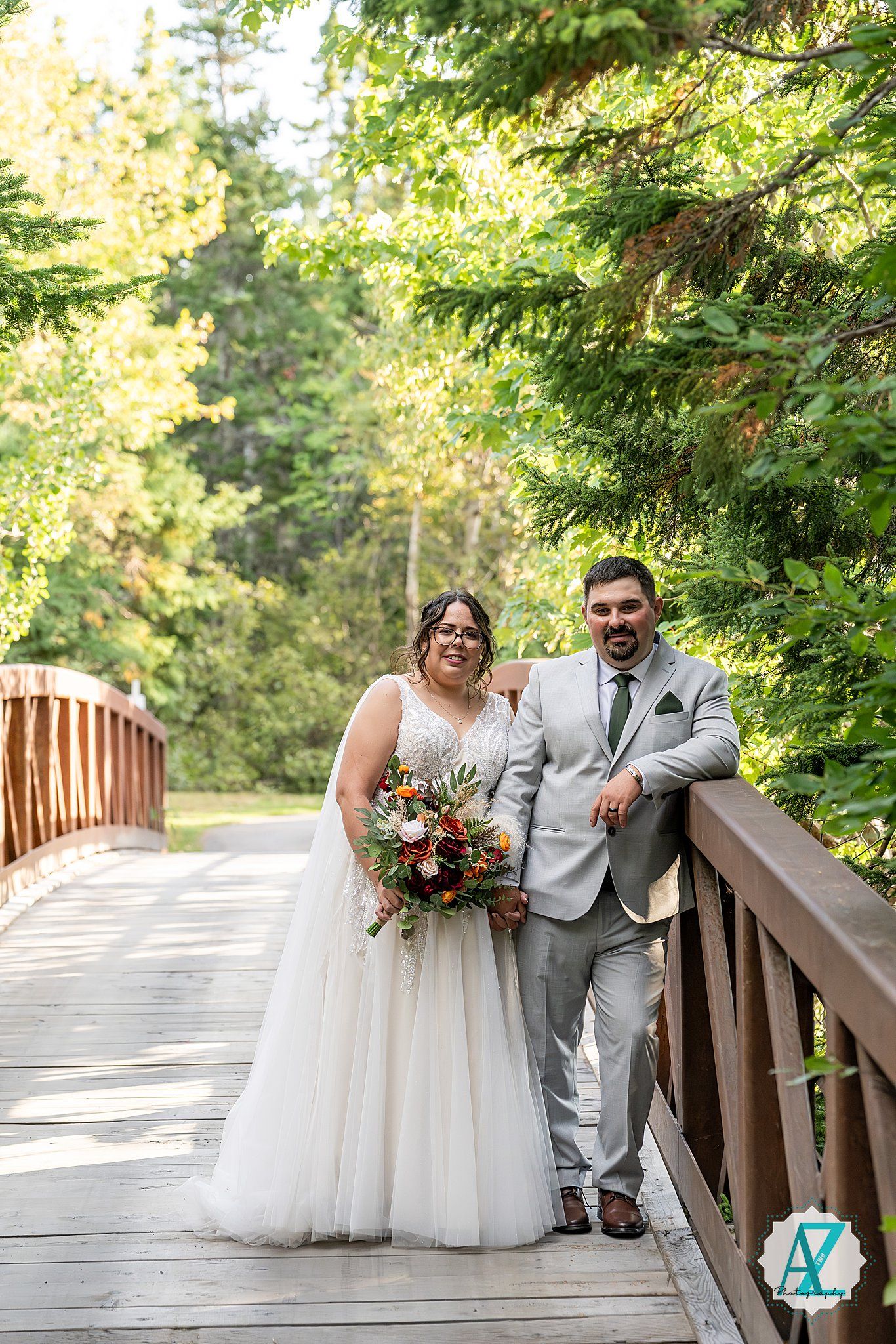 A couple in classic wedding attire share a romantic moment on a scenic wooden bridge surrounded by lush greenery.