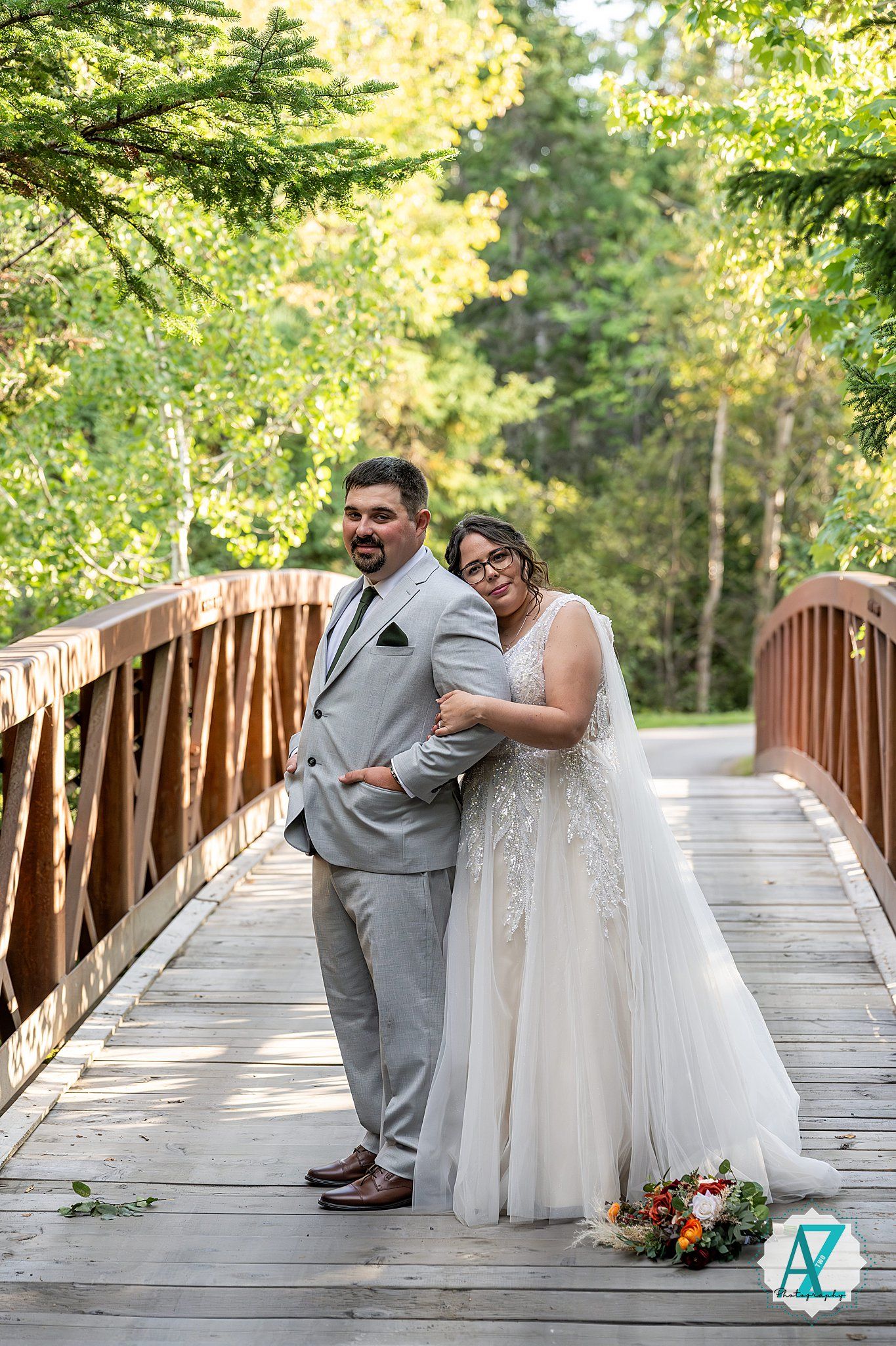 Couple poses playfully on wooden bridge surrounded by lush greenery in series of romantic wedding photos.