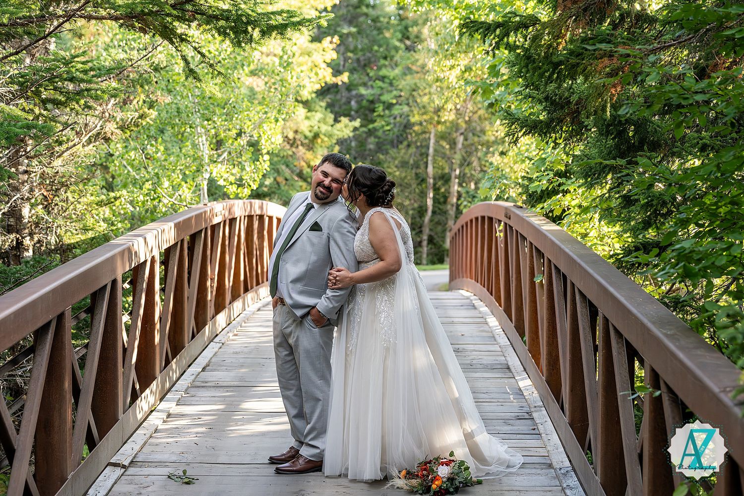 Couple sharing romantic moments on a wooden bridge surrounded by lush green forest scenery.