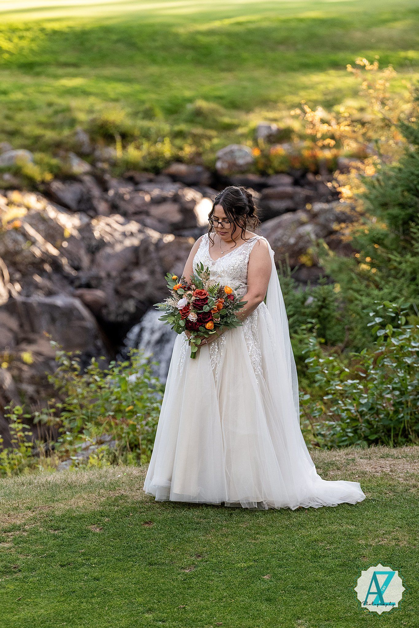 A flowing white wedding dress billows in the breeze against a backdrop of rocks and greenery during an outdoor photo session.