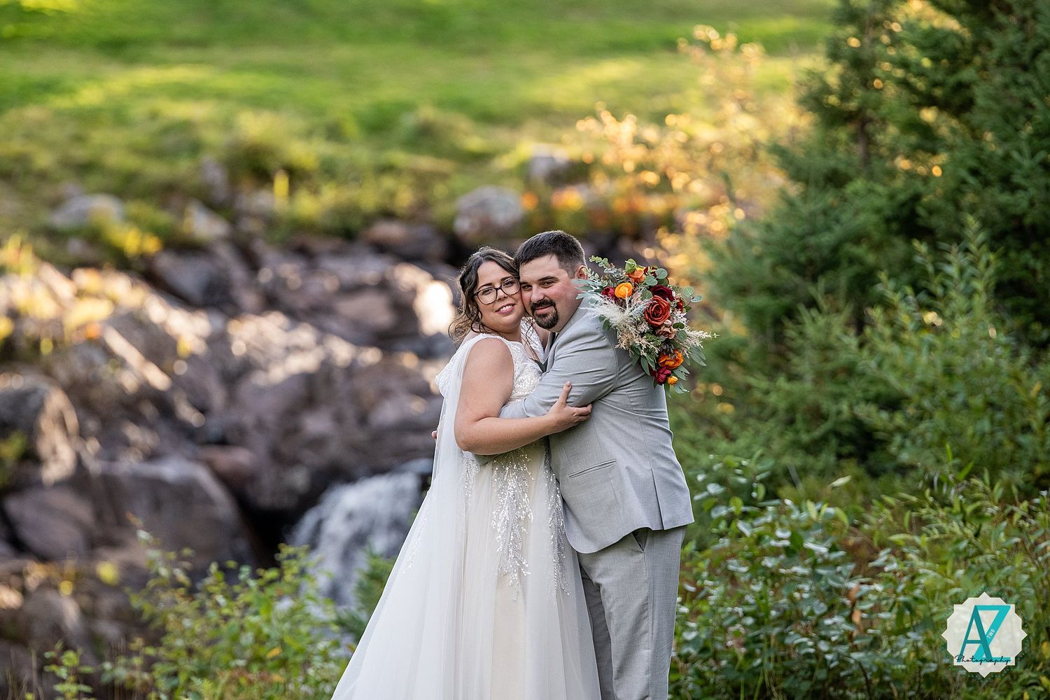 A couple in formal wedding attire shares romantic moments by a waterfall in a lush outdoor setting.