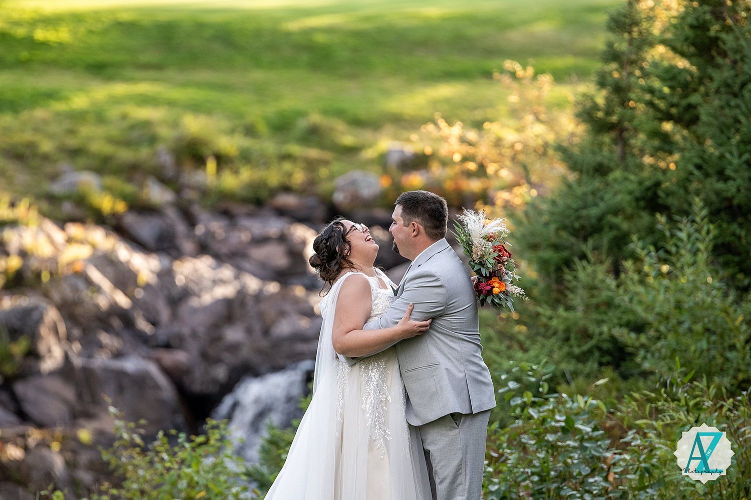 Newlyweds share intimate moments on rocky terrain with trees and natural scenery in background.