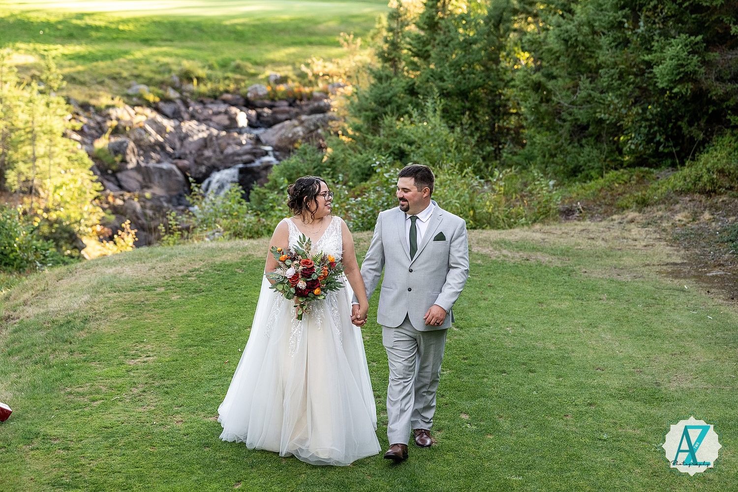 A couple walks hand in hand across a verdant lawn with rocky mountain terrain in the background during their wedding day.