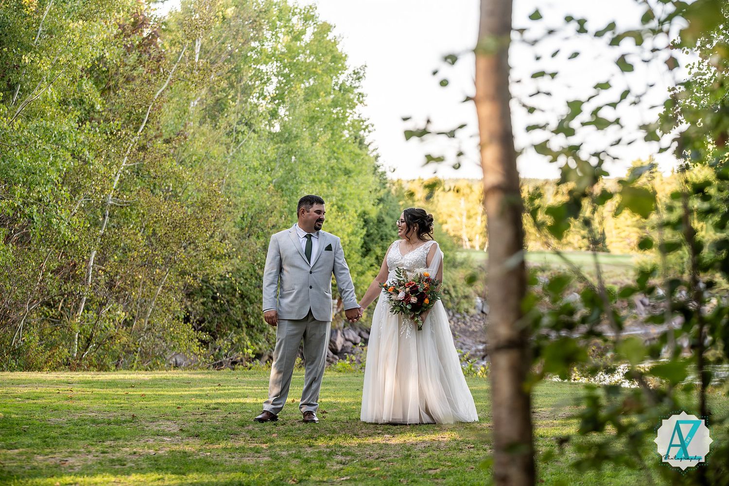 Couple in wedding attire having tender moments among trees in a sunlit forest setting.