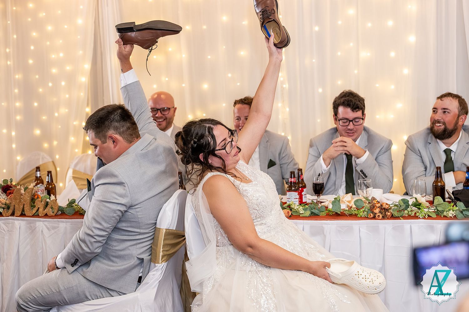 Wedding guests celebrate and raise their glasses during a reception under twinkling string lights.
