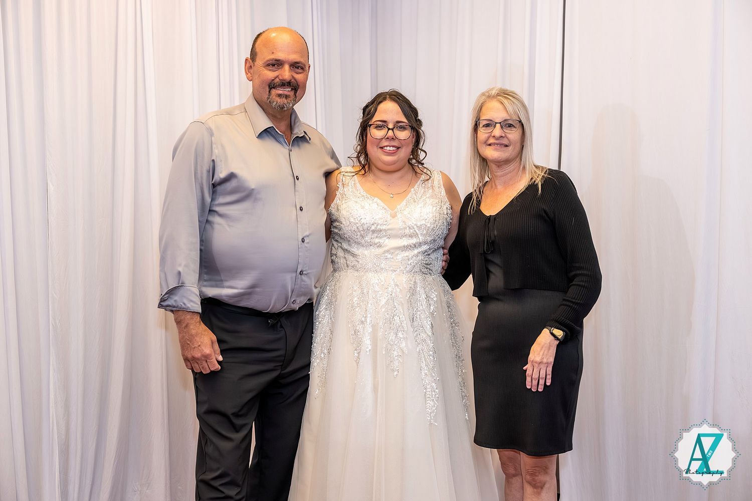 Wedding party members pose together wearing formal attire in white and black at an indoor venue.