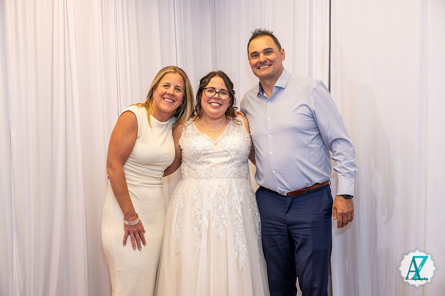 Three people stand close together posing for a special occasion photo against a white curtain backdrop.