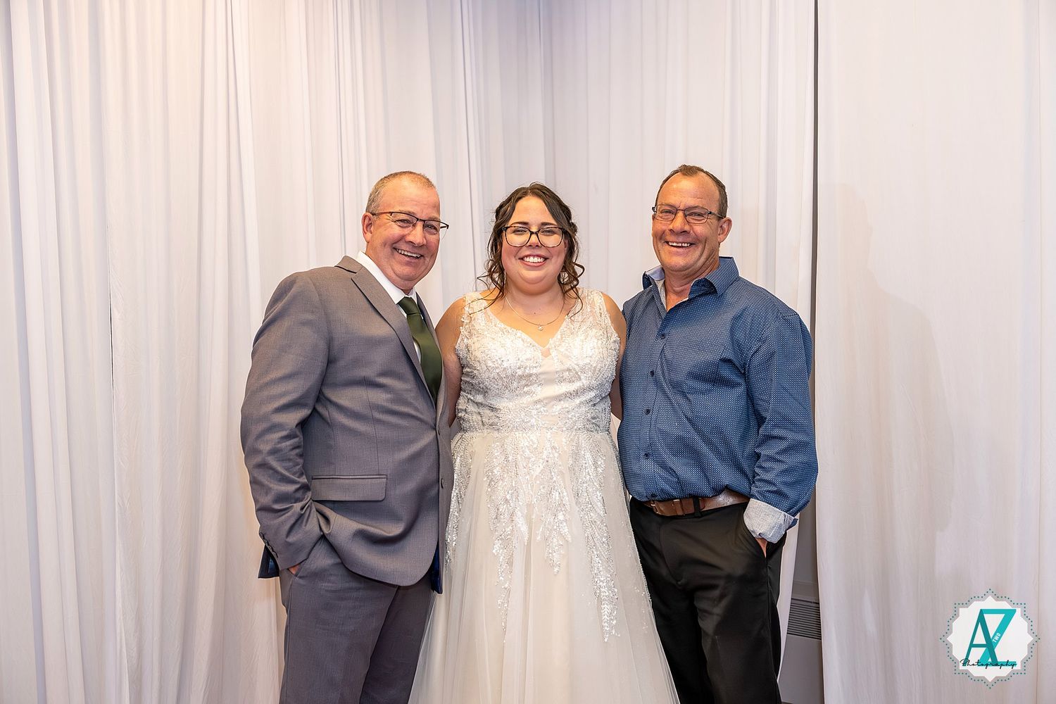 Three formal wedding guests pose together against a white backdrop at a celebratory event.