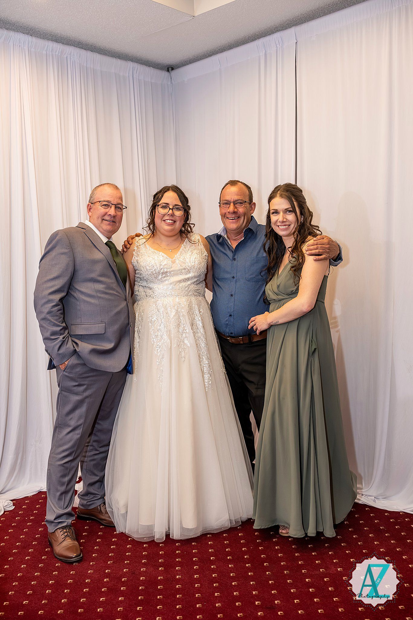 Wedding party group poses together in front of white curtain backdrop wearing formal attire.