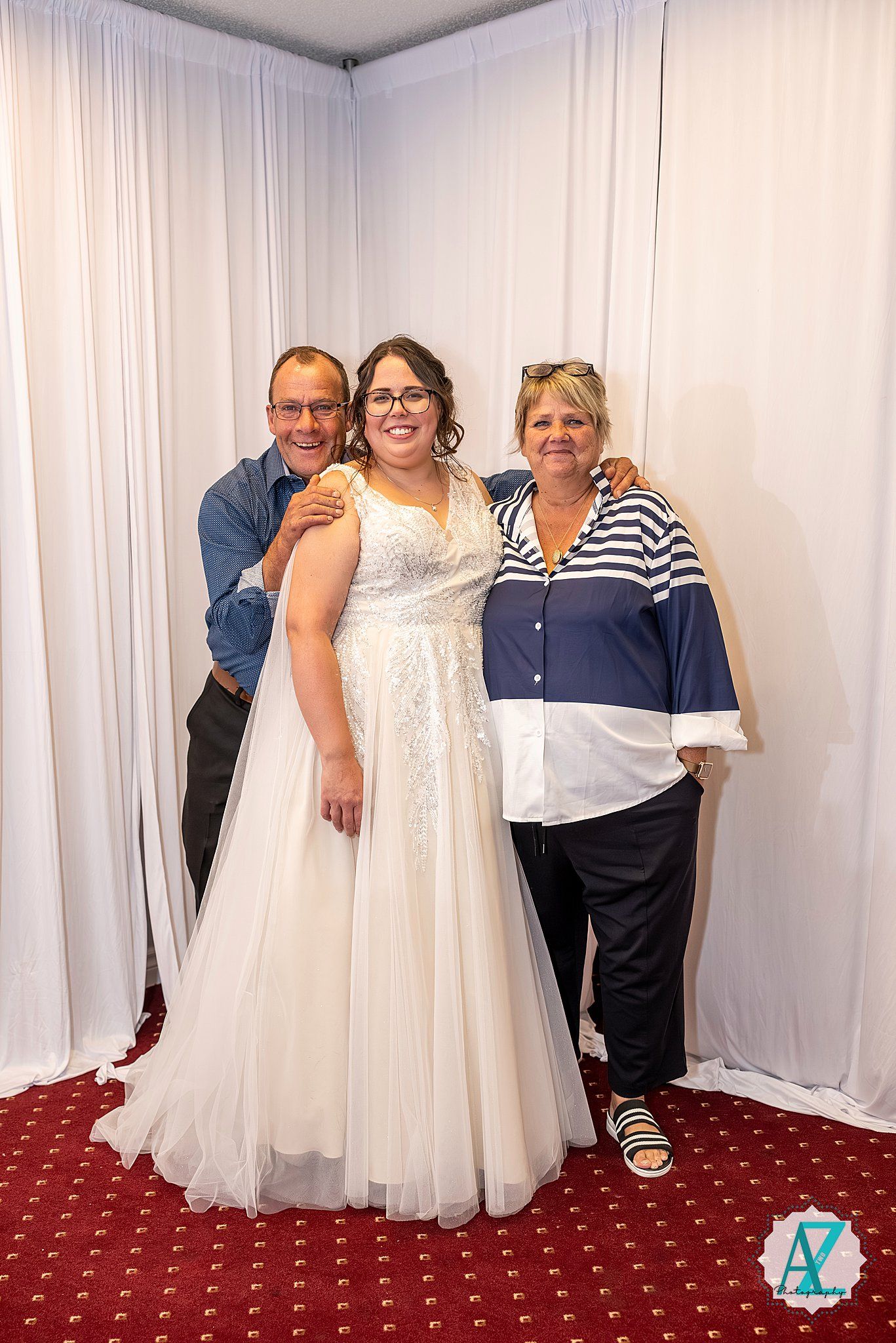 A group poses together in a room with white curtains and red carpeting at a formal event.