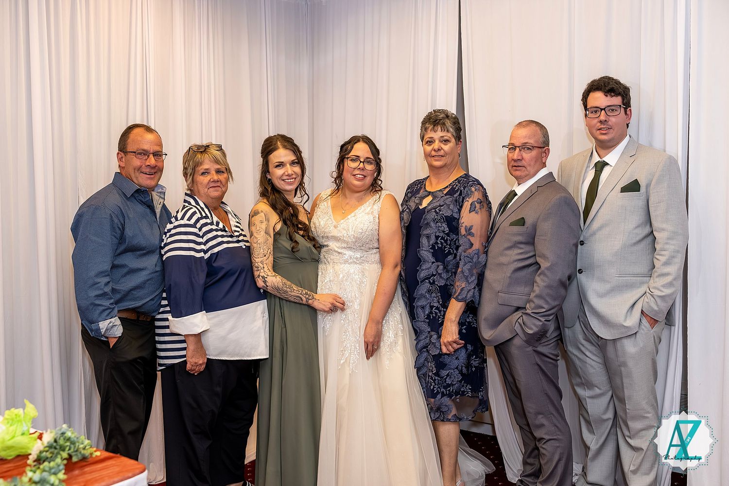 A group of formally dressed people pose together against a white curtain backdrop at a special event.