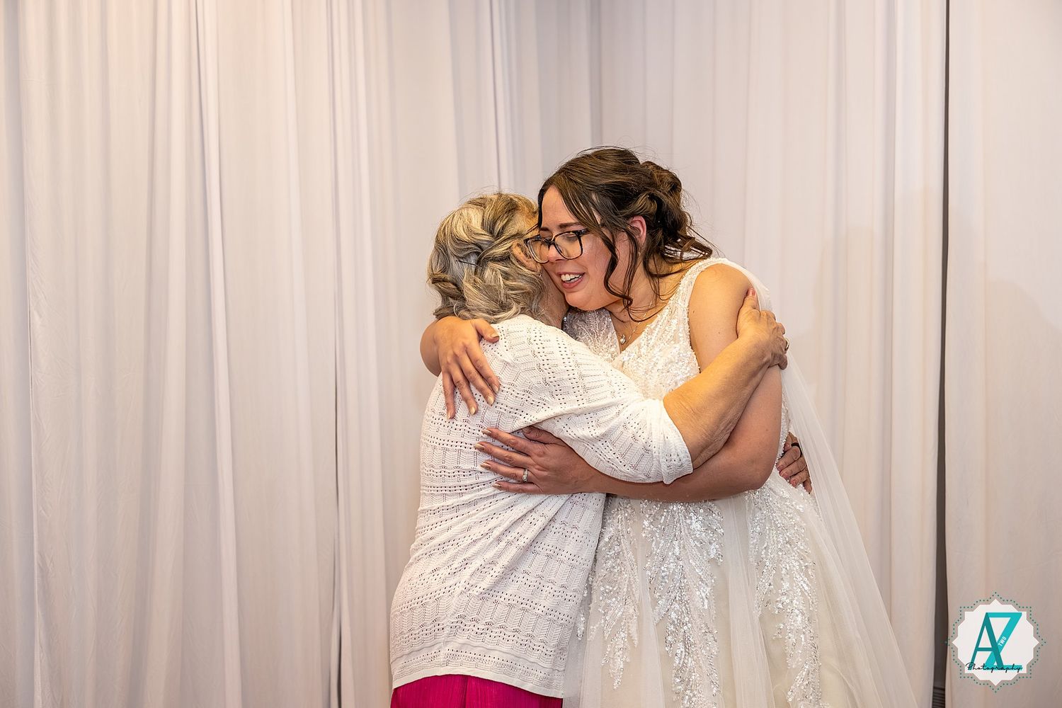 People embrace and pose for photos in front of a white curtain backdrop at a formal gathering.