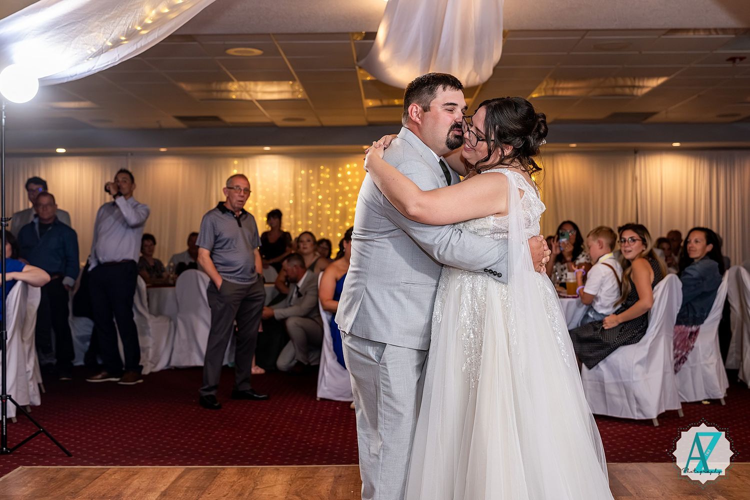 Wedding couples share romantic first dances in an elegant ballroom reception venue set with romantic lighting.
