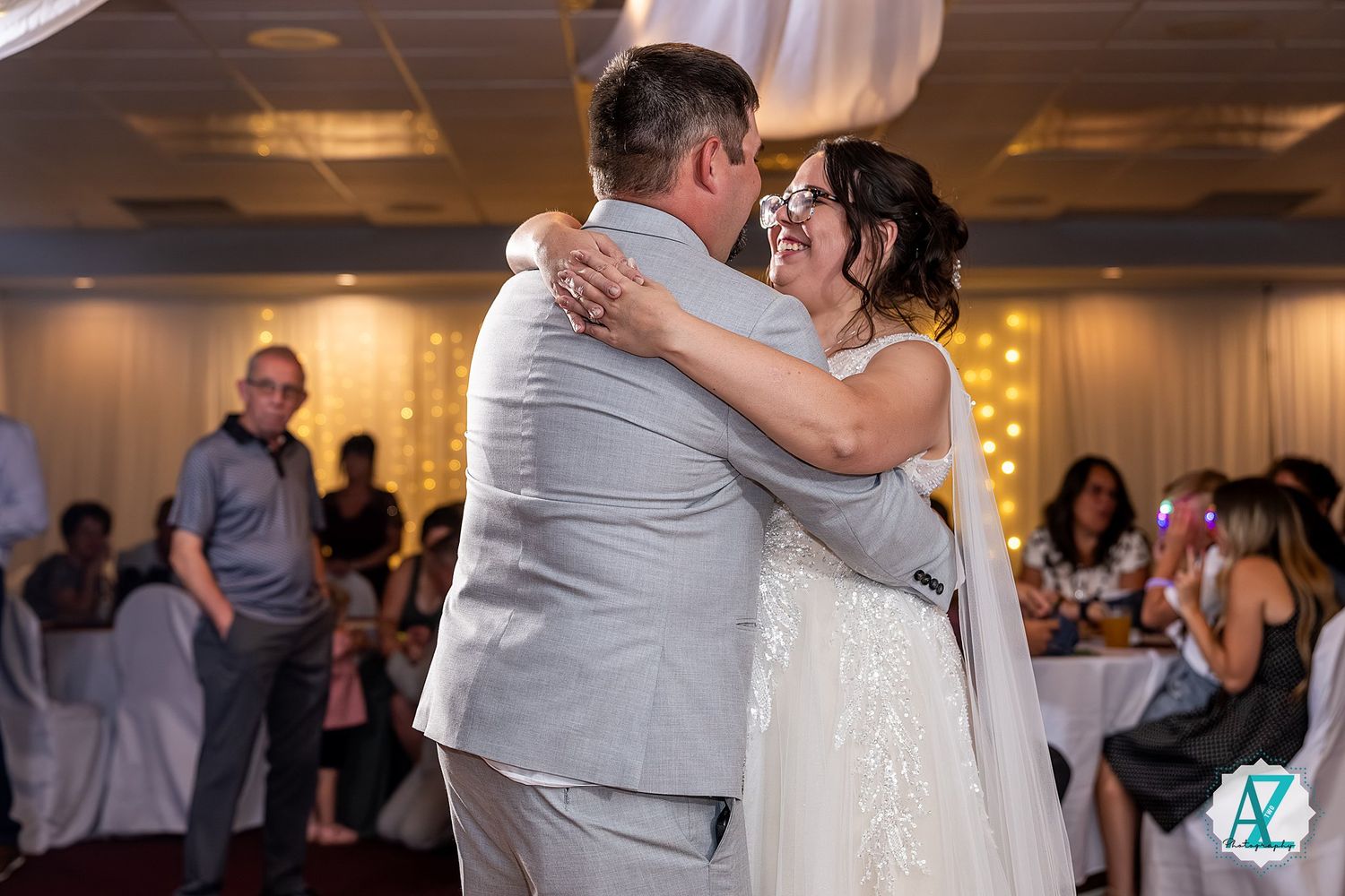A couple shares their first dance as newlyweds at an elegant indoor wedding reception surrounded by guests.
