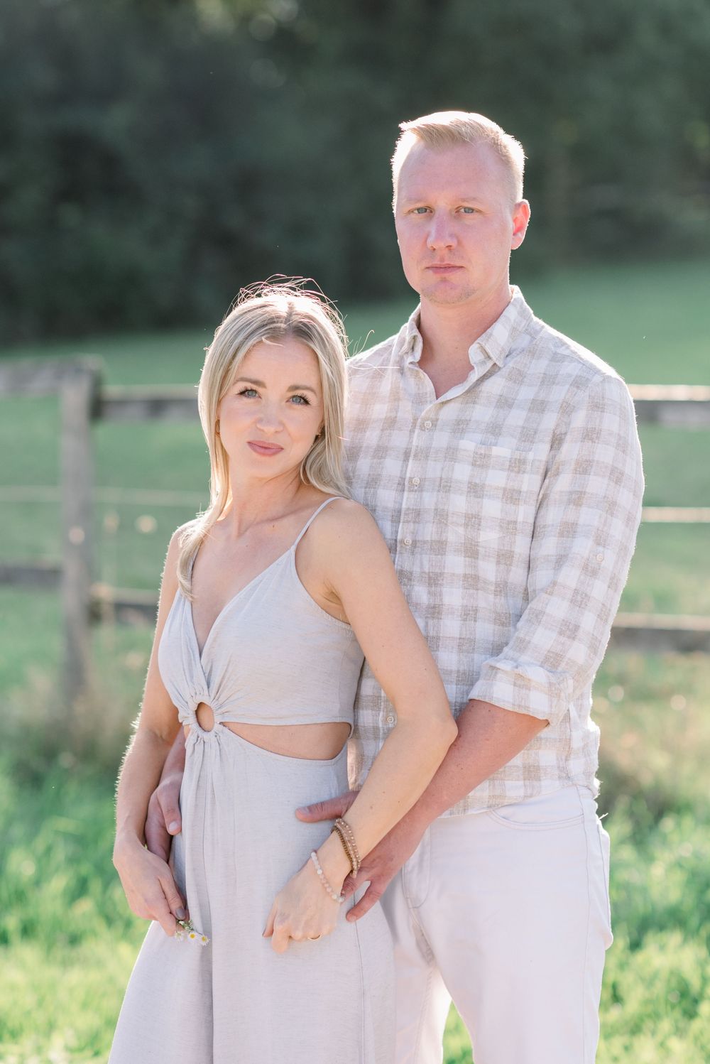 Couple embracing in casual attire against a natural green background.