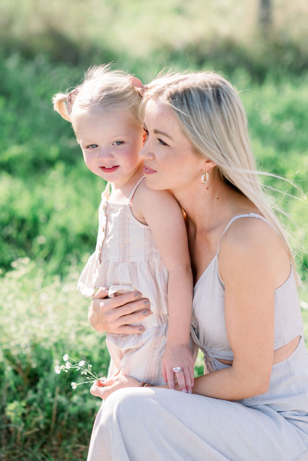 Intimate family moment captured outdoors with soft natural lighting and green background.