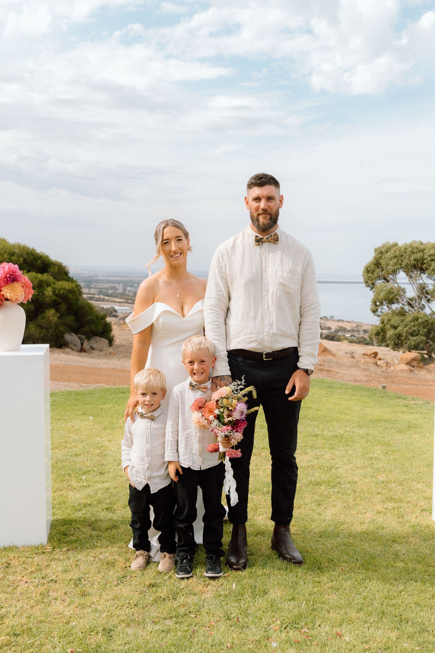 A family group poses together on a grassy hilltop overlooking a scenic view.