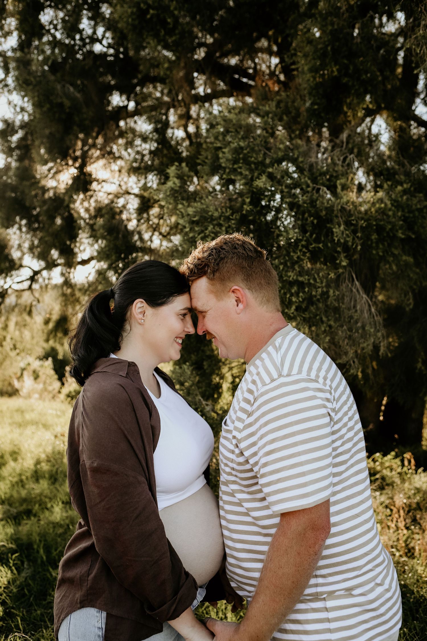 A romantic couple shares tender moments in a sunlit forest setting wearing brown and striped clothing.