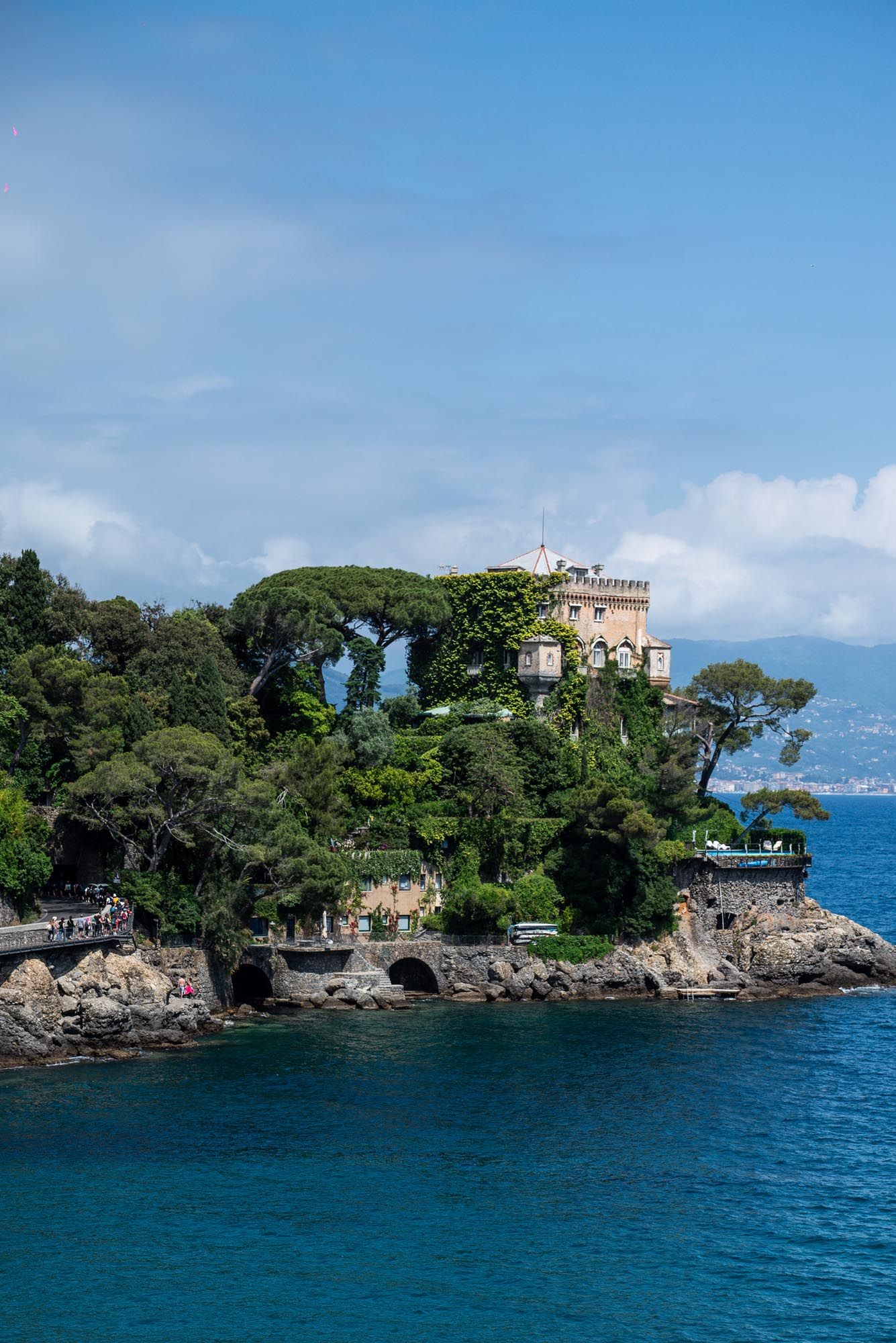 A historic castle perched on a rocky cliff overlooking the blue Mediterranean Sea in Portofino, Italy.
