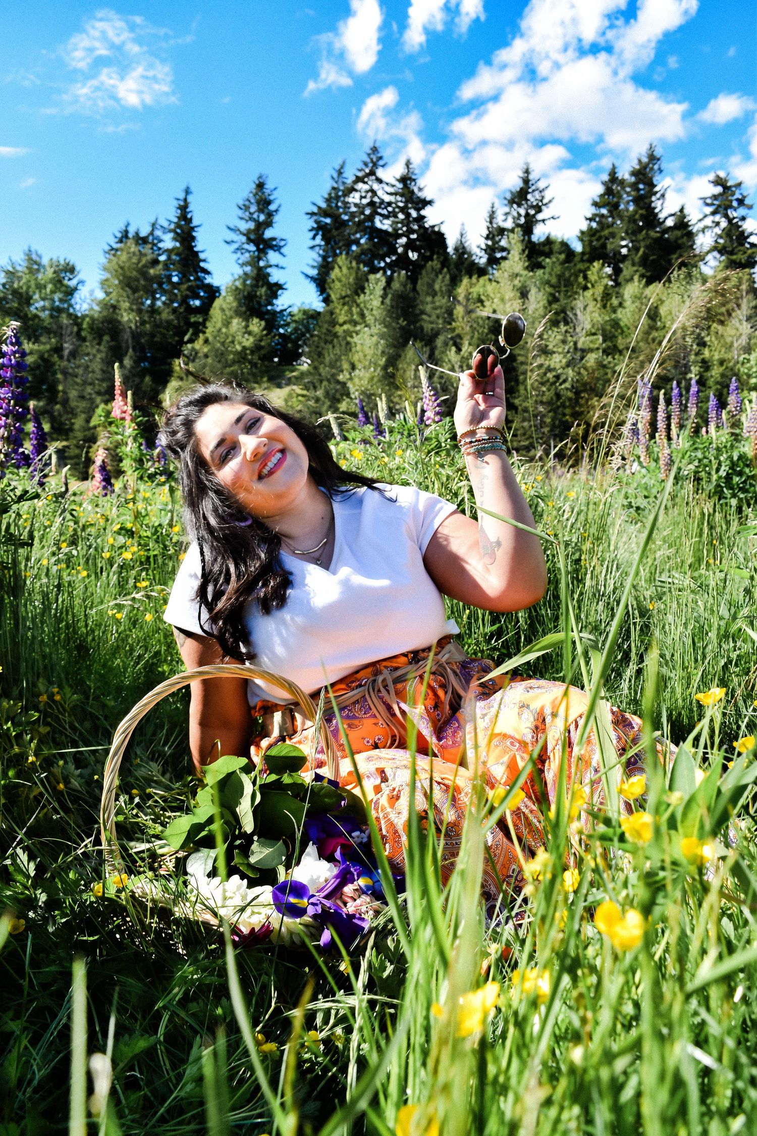 Seattle senior girl sitting in a wildflower field with basket of flowers and sunglasses during graduation portraits.