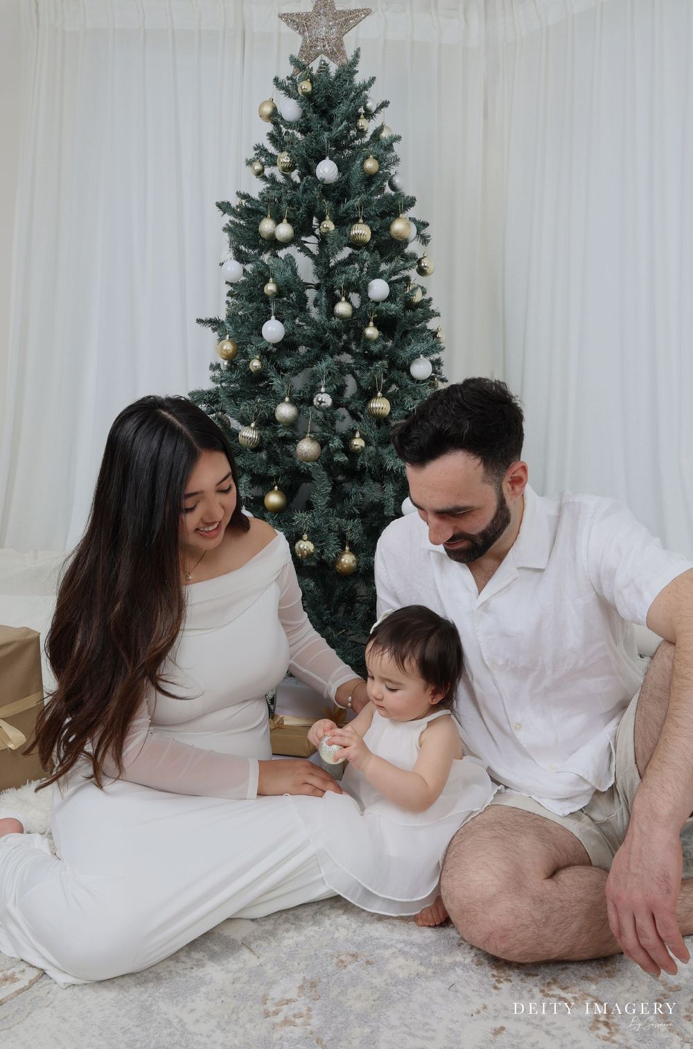 A family in white outfits sharing precious moments together while sitting in front of a decorated Christmas tree.