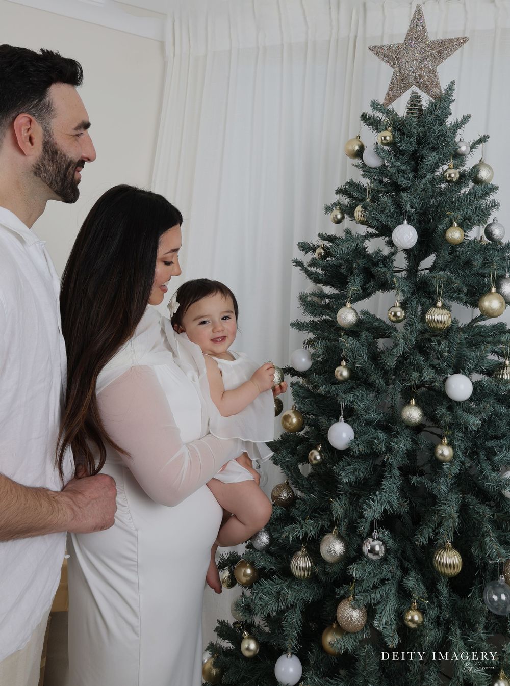 Modern family gathered around a decorated Christmas tree with white, silver and gold ornaments during holiday season.