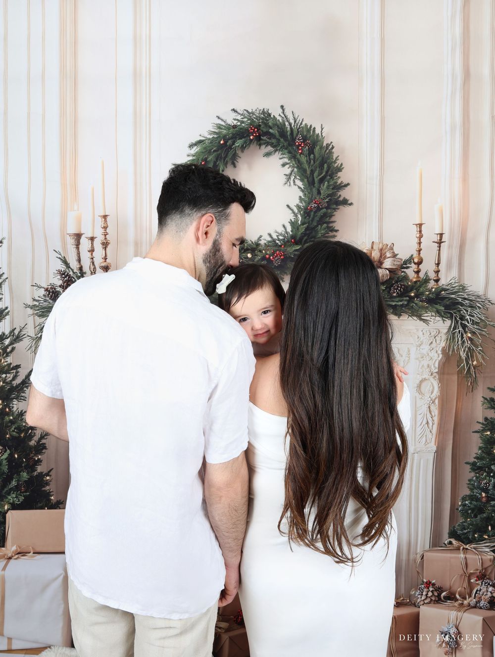 A couple shares an intimate moment while decorating for Christmas with a pine wreath and candlesticks in the background.