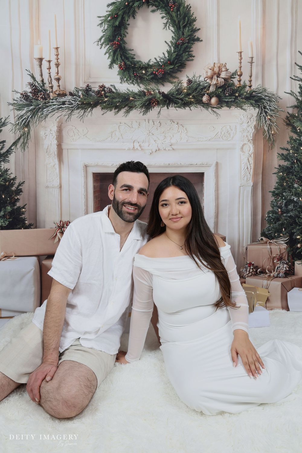 A romantic holiday photo session featuring a couple in matching white outfits posing on a white couch with Christmas decor.