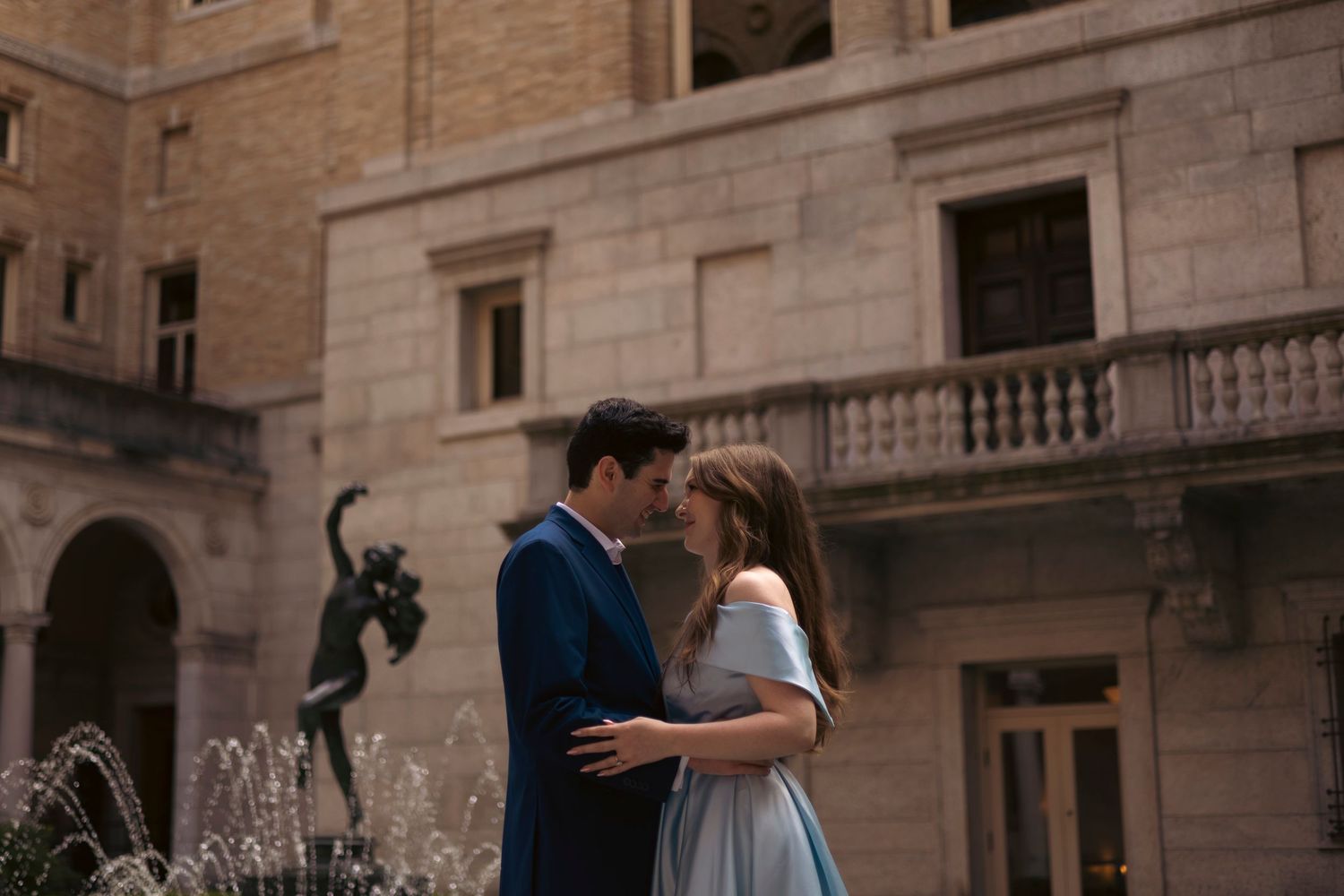 Dancing couple performs ballet poses while photographers capture their movement in front of a grand stone building.