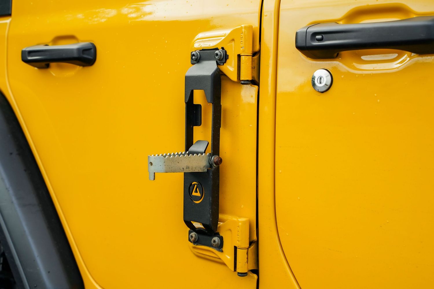 Close-up of yellow Jeep's door panels showing hinges and black hardware.